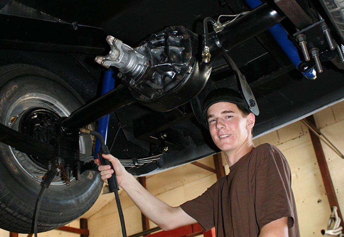 A Future Men apprentice working under a truck at a local shop