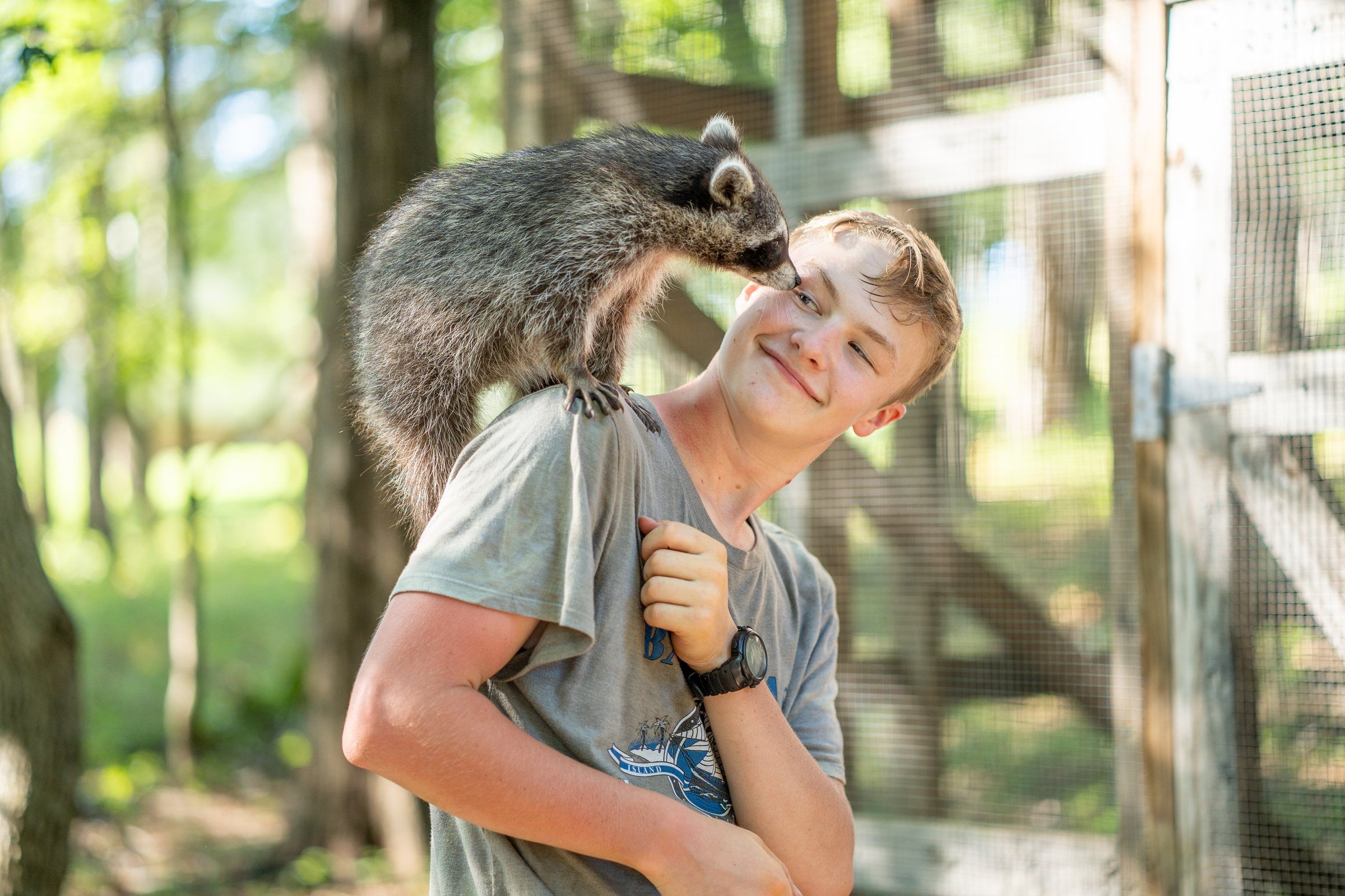 A smiling Future Men student with a rehabilitated raccoon on his shoulder
