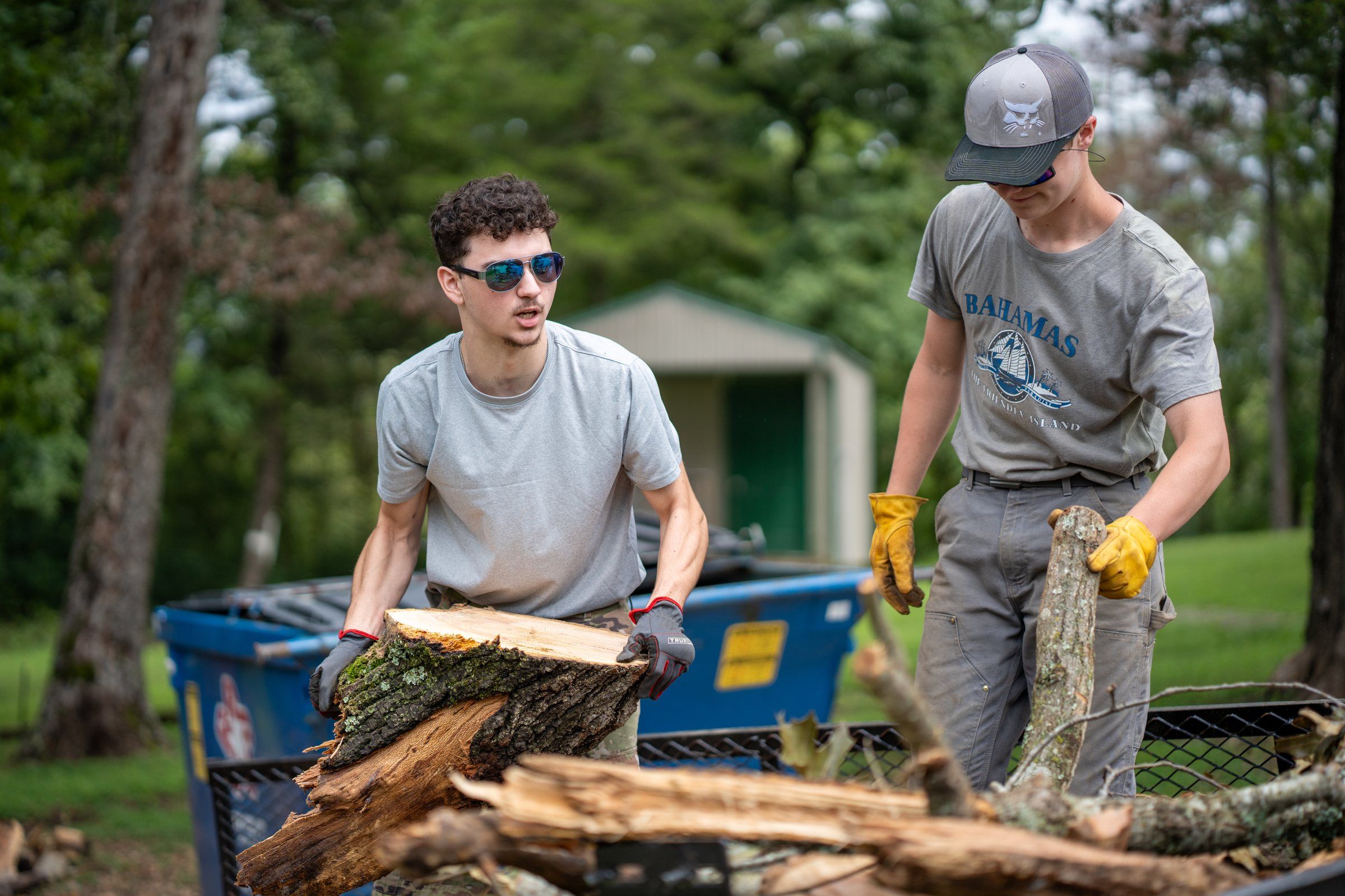 Two Future Men students hauling split firewood to a cart on campus